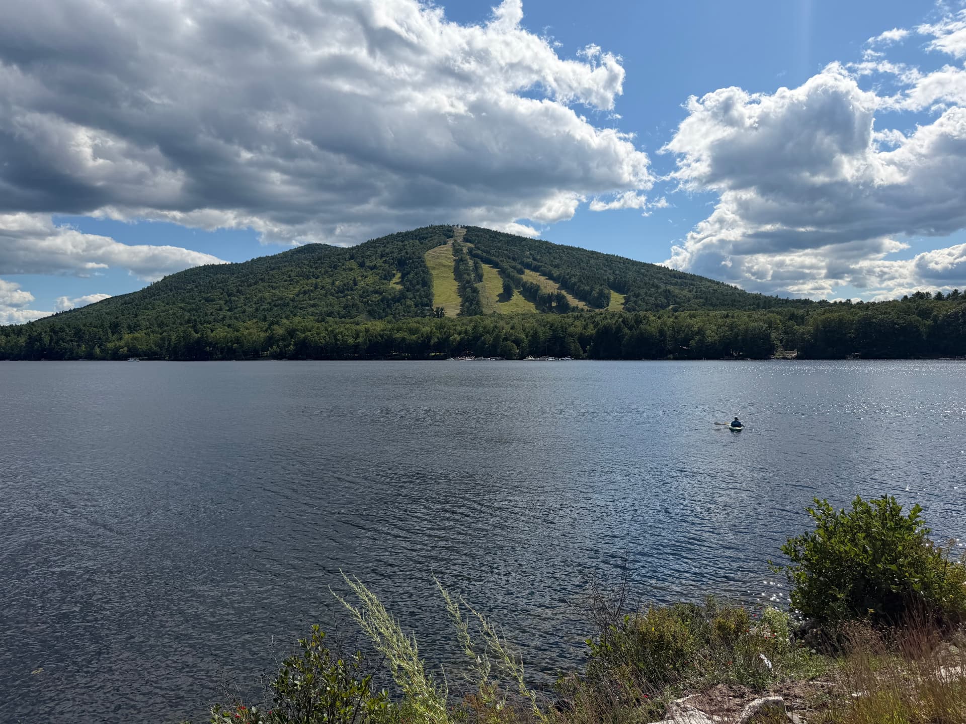 A serene lake and forested mountain under a wide sky in the Lakes Region of Maine